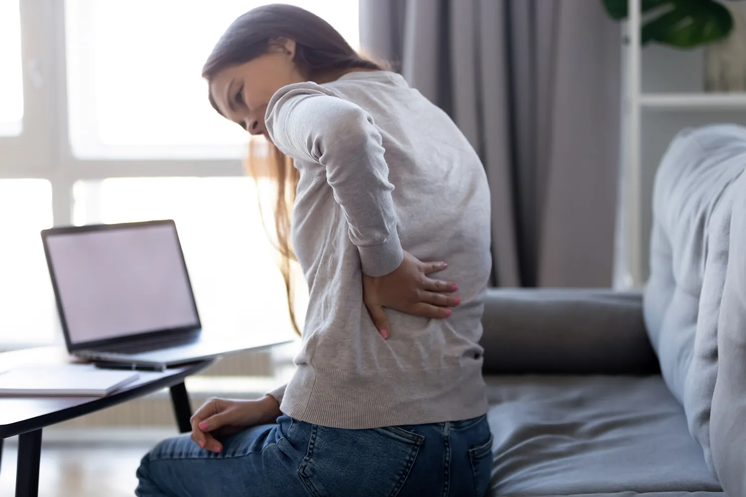 Woman holding her lower back while working at a laptop